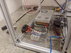 Thumbnail: The rear electronics enclosure mounts the mains-voltage components, including the power input jack (with button and fuse), the 24V switching power supply, and the solid-state relay responsible for switching the AC-powered bed heater
